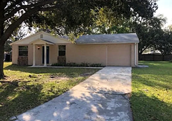 Single-level stucco home with a front-facing garage and shade oak in Orange Park, Florida